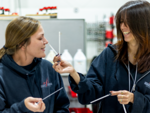 Two AFI lab techs smell fragrance on a blotter strip while smiling